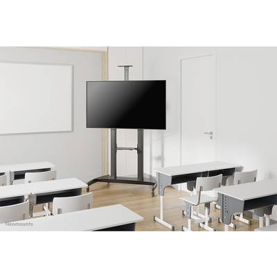 Une salle de classe vide avec des tables et des chaises blanches. Un grand écran noir monté sur un support mobile est placé à l'avant, à côté d'une porte fermée.