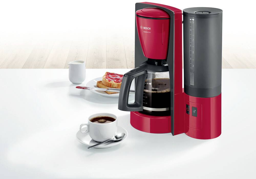 Machine à café rouge avec une carafe pleine de café sur une table. À côté, une assiette dressée avec du toast et une tasse de café.