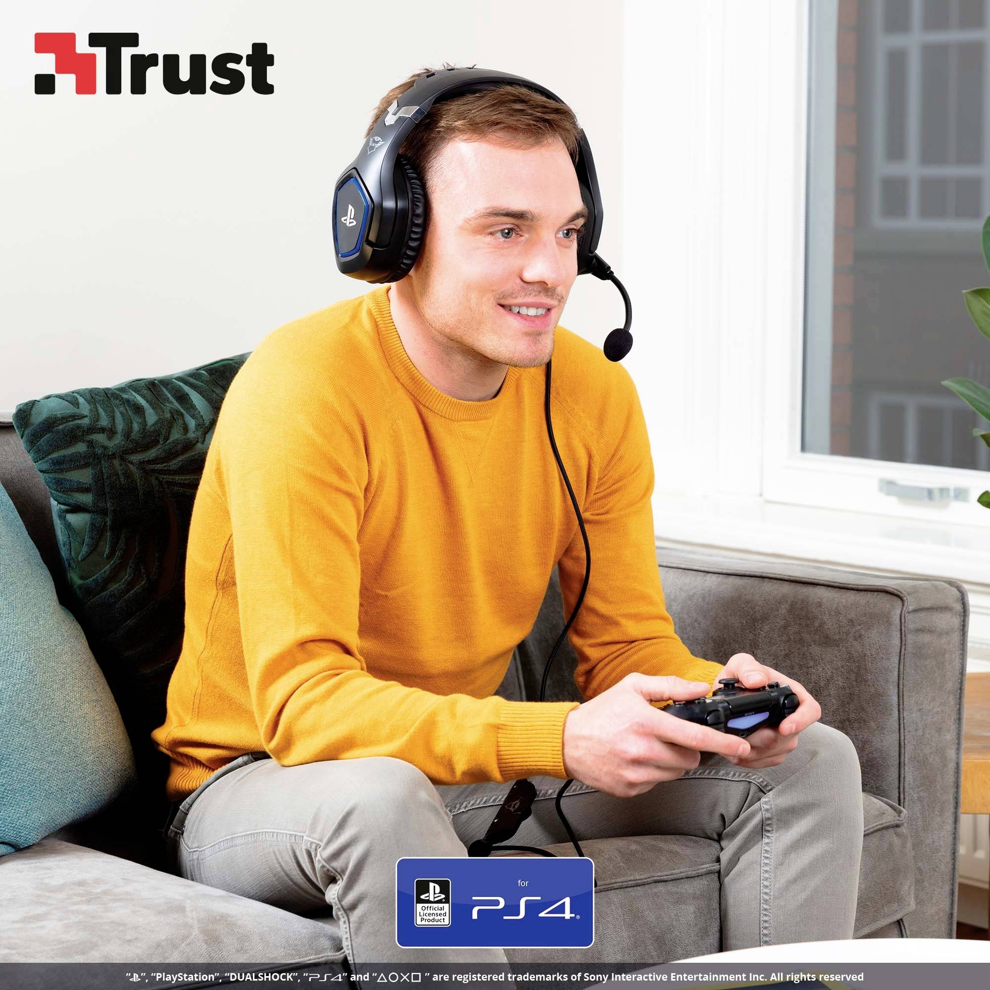Un homme portant un casque est assis sur un canapé, tenant une manette et regardant un écran. Le logo 'Trust' est situé en haut à gauche.