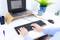 Des mains tapent sur un clavier d'ordinateur posé sur un bureau blanc. En arrière-plan, un ordinateur portable, une tasse et une plante.