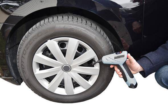 Une personne vérifie la pression d'un pneu de voiture à l'aide d'un gonfleur numérique sur un véhicule noir.