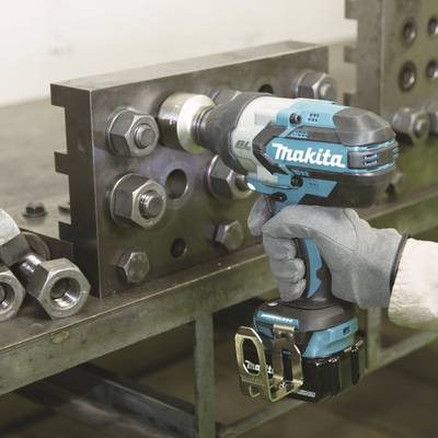 Une personne portant des gants utilise un tournevis sans fil bleu pour serrer un grand écrou métallique sur un établi.