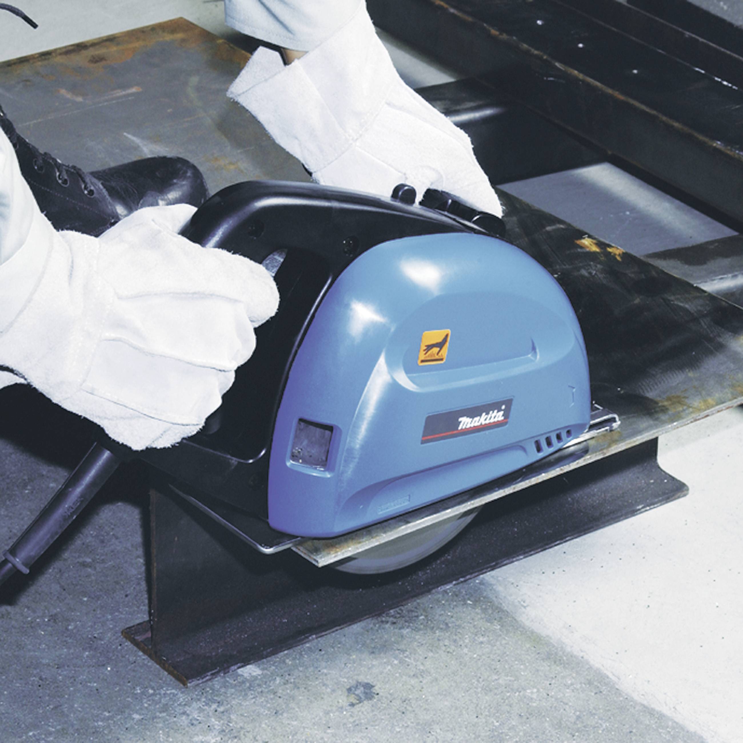 Une personne coupe du métal avec une scie industrielle bleue dans un atelier. L'accent est mis sur la précision du travail.