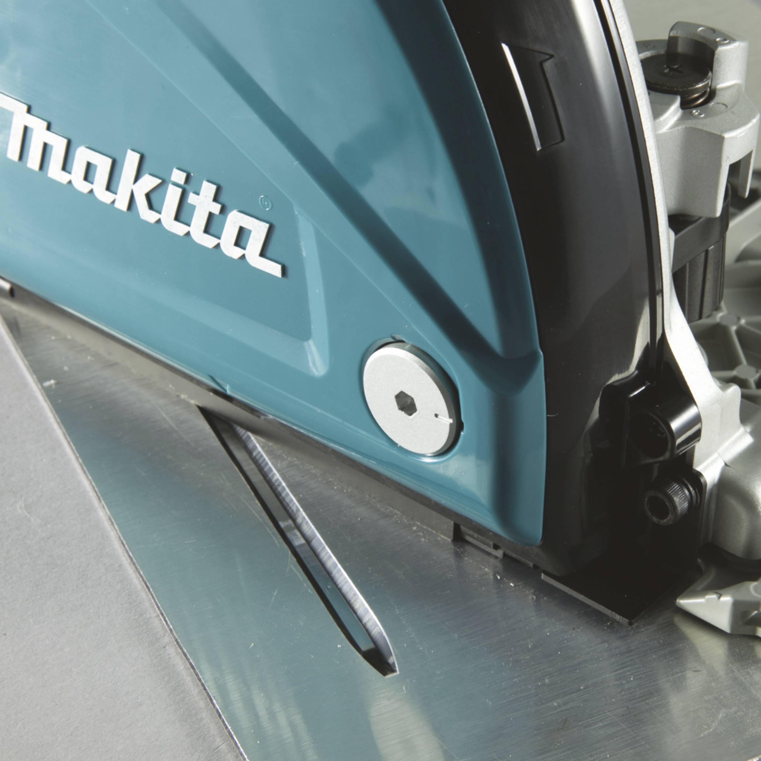 Une scie circulaire en gros plan avec une lame de scie visible et un boîtier bleu portant le logo 'Makita'. L'outil en action sur une surface métallique.