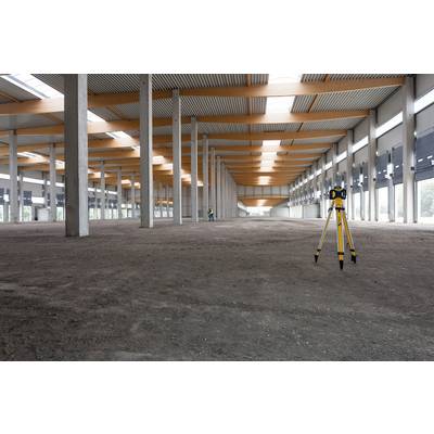 Un espace intérieur vaste et vide avec des piliers en béton et des poutres en bois au plafond. Un instrument de mesure est placé au premier plan.