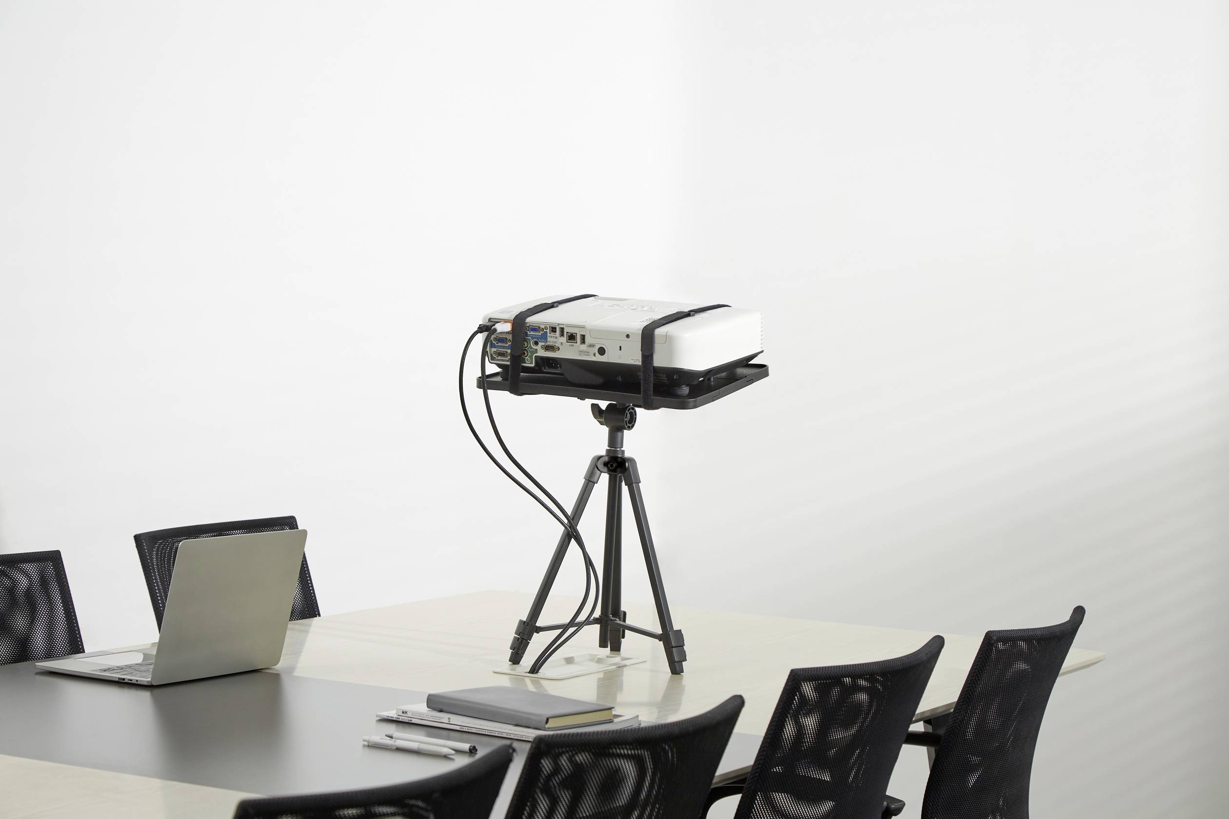 Un projecteur est posé sur une table dans une salle de conférence, entouré de plusieurs chaises vides et d'un ordinateur portable.