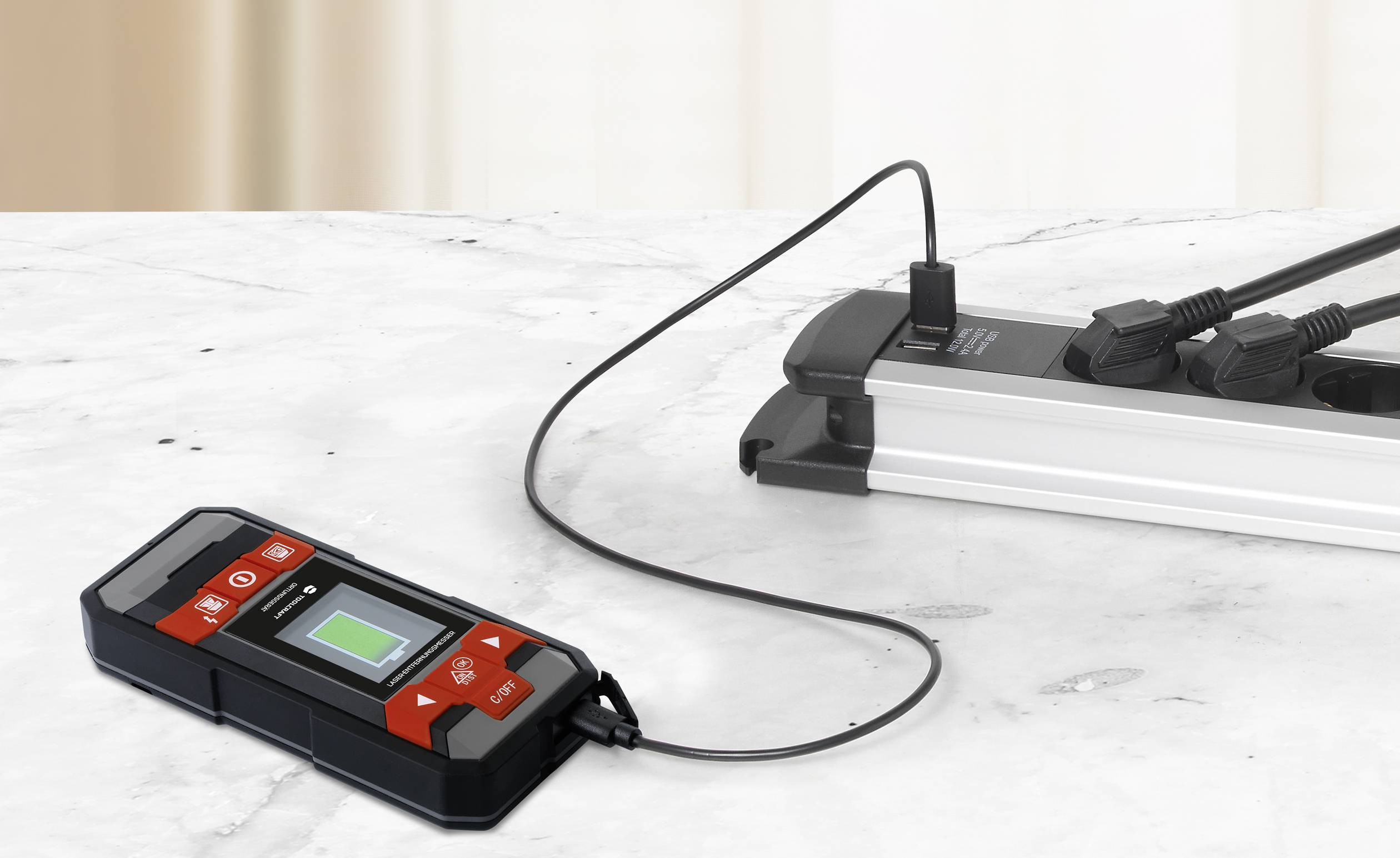 Un appareil noir avec un panneau de commande rouge, relié à un appareil de mesure électrique, est posé sur une table en marbre.