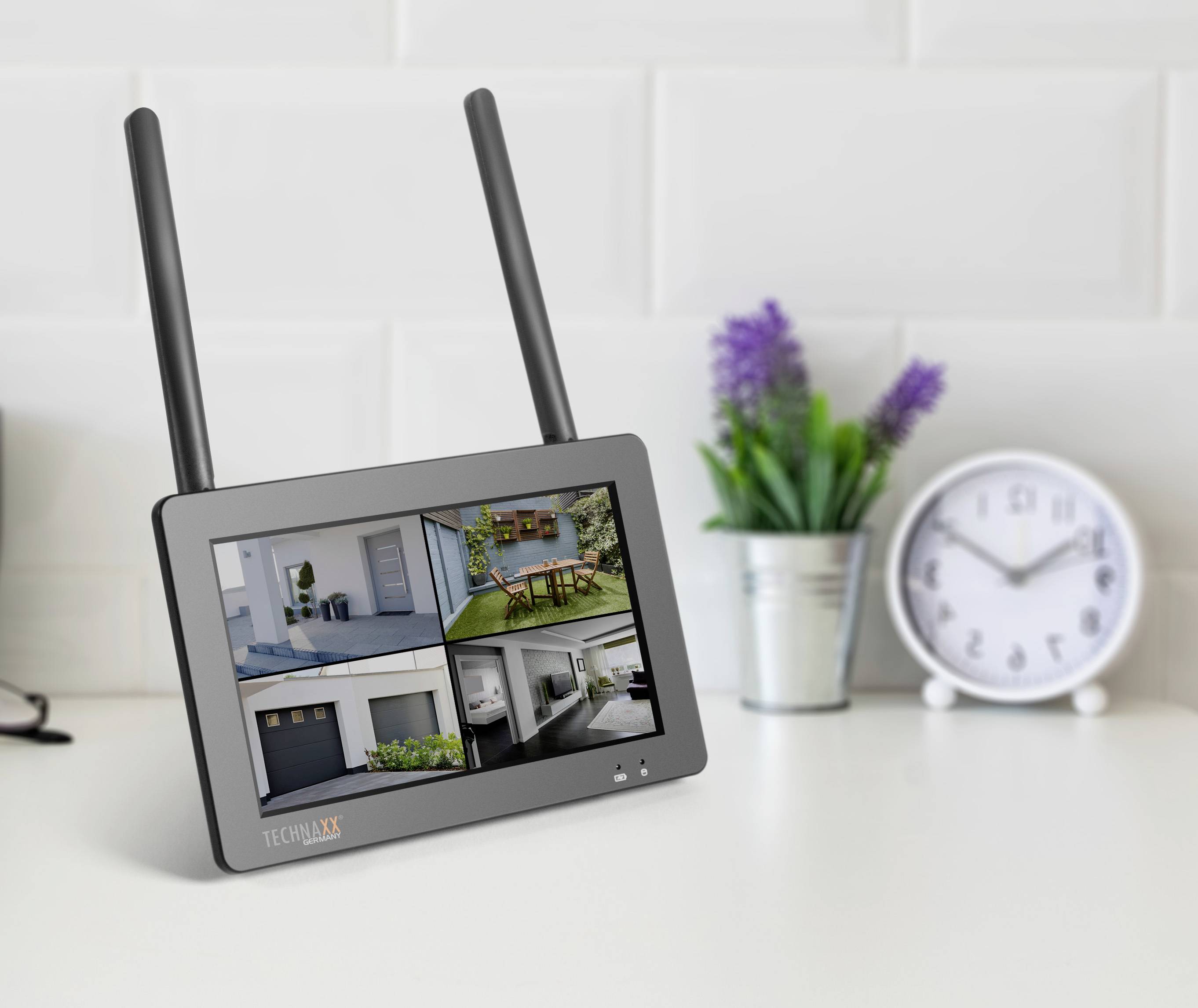 Un écran doté de deux antennes affiche des flux de caméras de surveillance, notamment un jardin, un garage et une pièce. Une horloge est visible en arrière-plan.