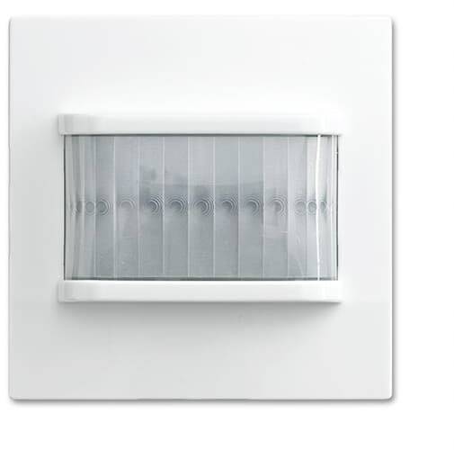 Un détecteur de mouvement blanc avec une fenêtre de visibilité texturée sur un mur blanc.
