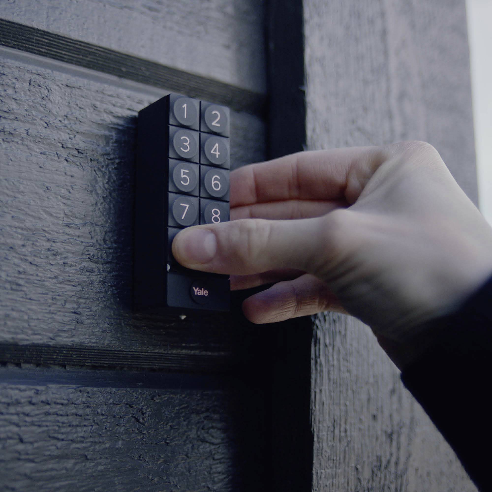 Une main entre un code sur un verrou électronique fixé à un mur en bois.