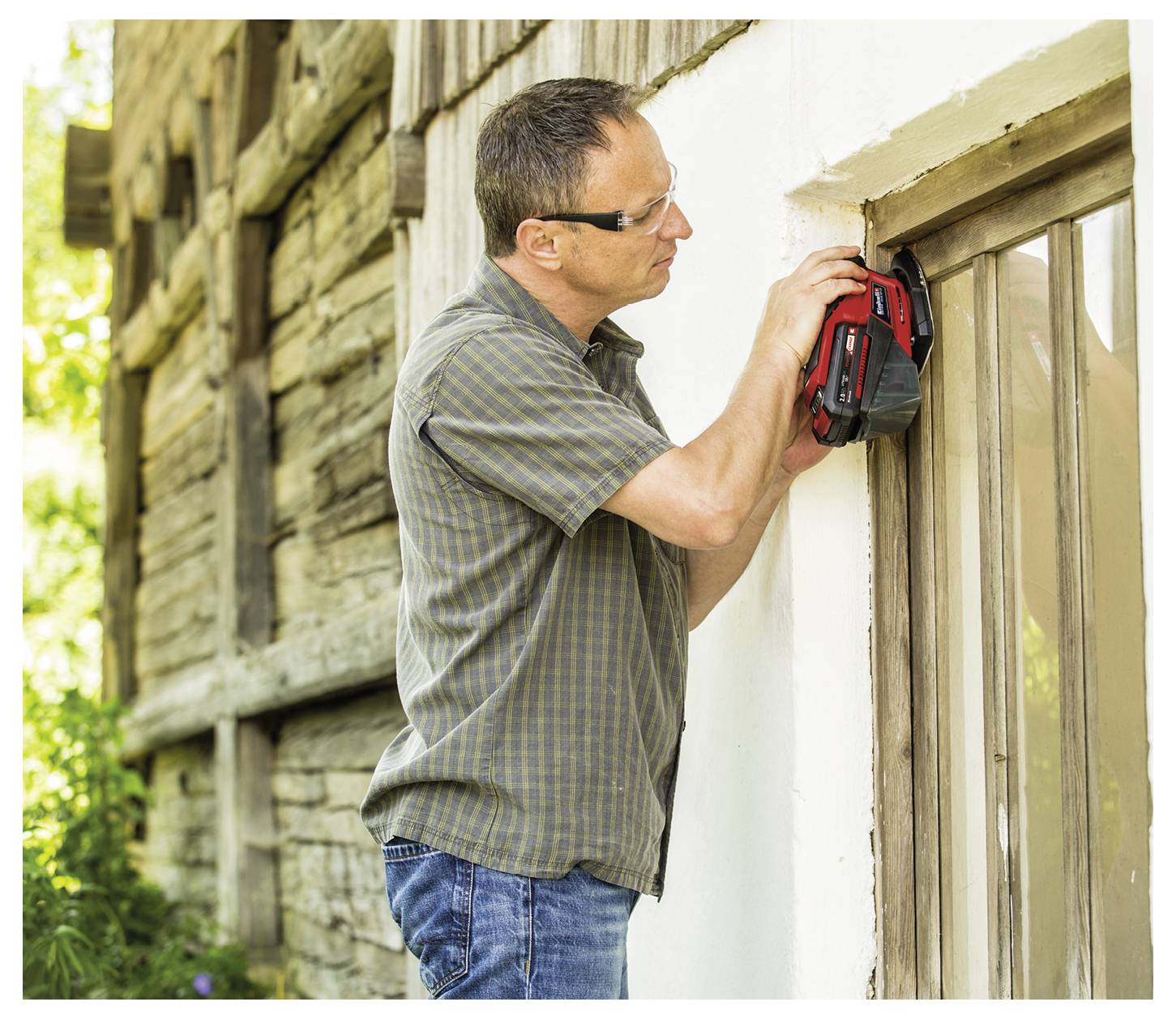 Un homme portant des lunettes utilise un appareil portatif pour inspecter le cadre de fenêtre en bois d'un bâtiment rustique, en se concentrant sur le coin supérieur.