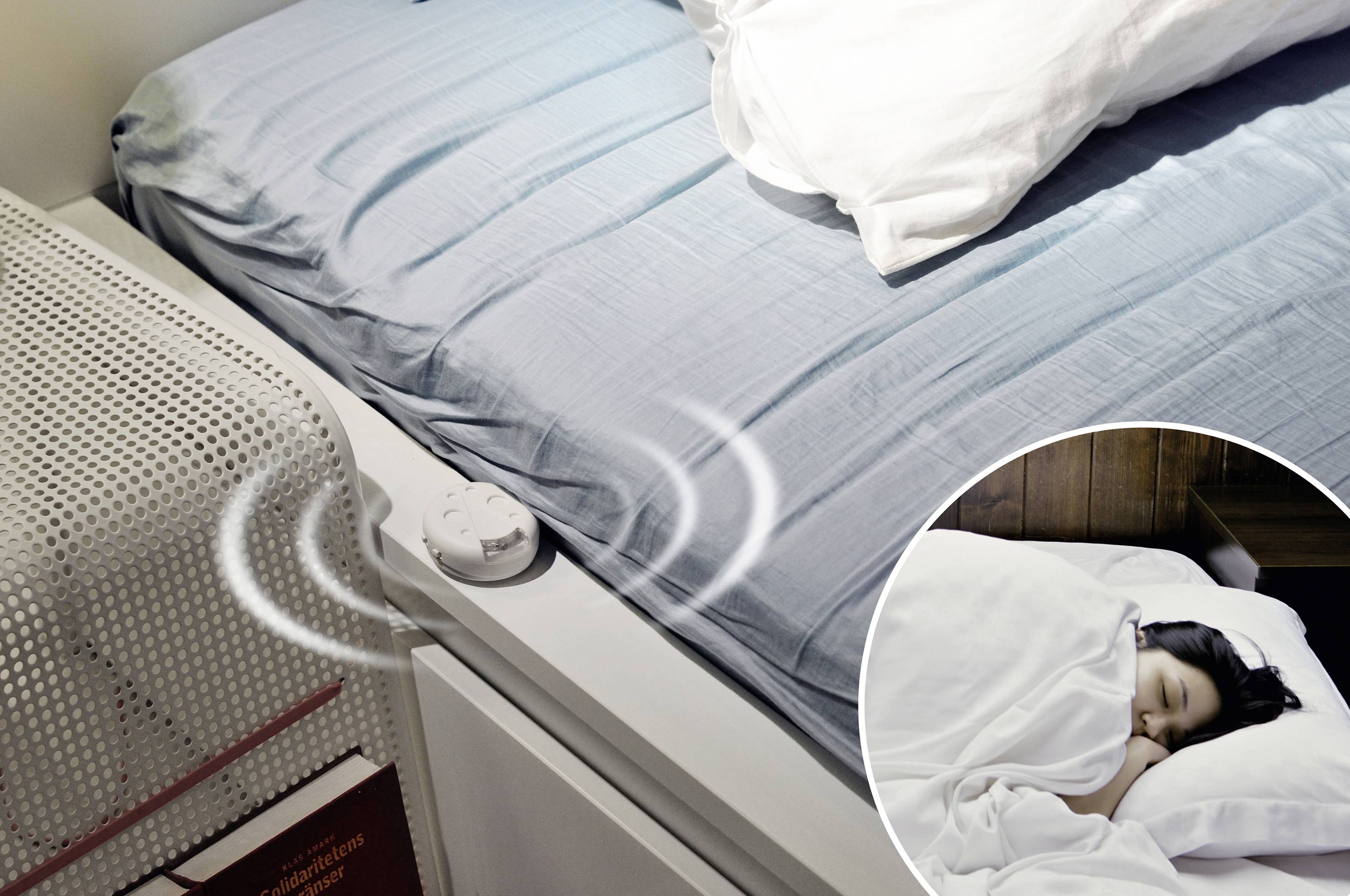 Un lit avec du linge de lit bleu. Un capteur d'activité sur la table de nuit. Dans la fenêtre circulaire, une personne dormant sous une couverture.