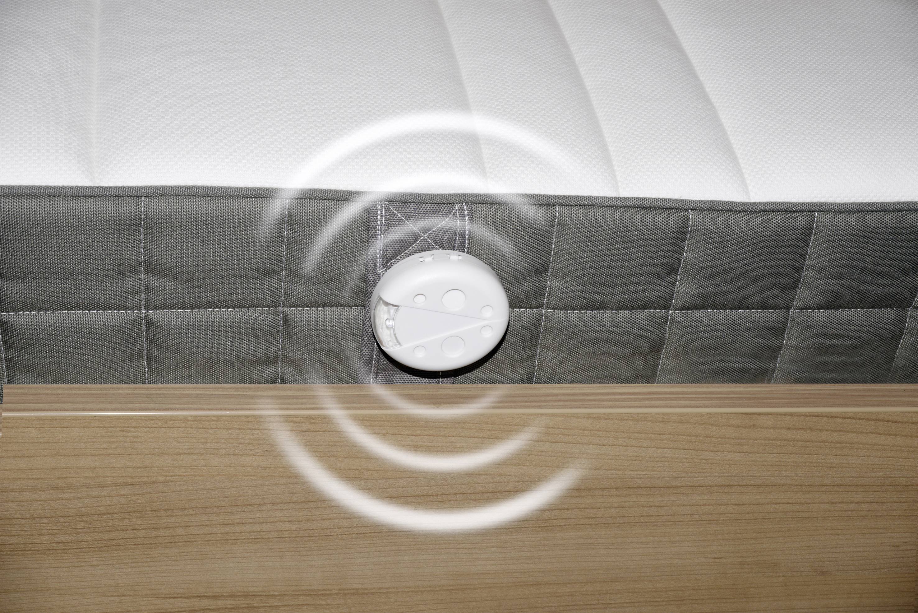 Matelas gris et blanc avec un capteur intégré qui émet des signaux sans fil. Châssis en bois visible.