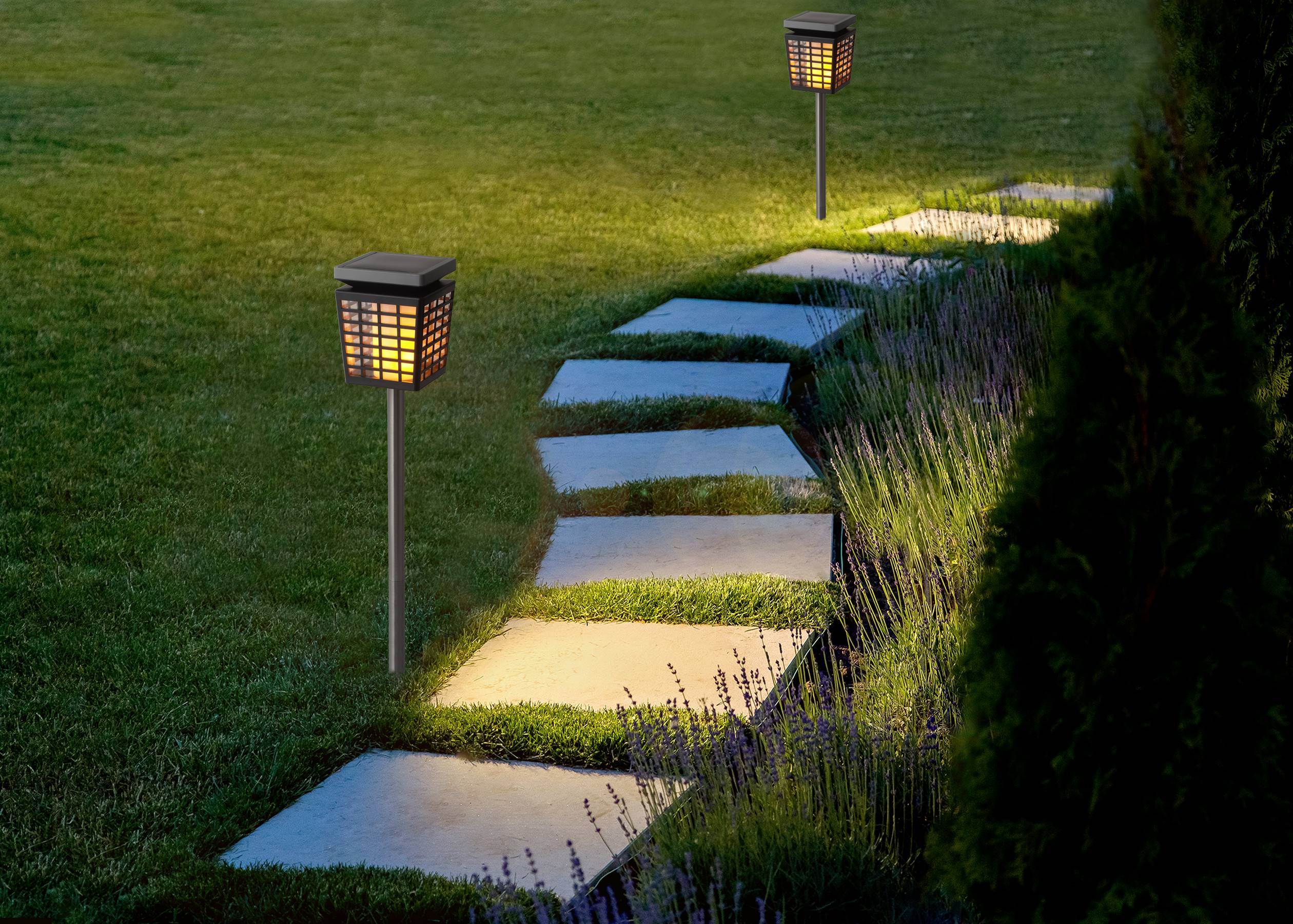Chemin de jardin dallé, bordé de lanternes décoratives illuminées. Le chemin traverse une pelouse.