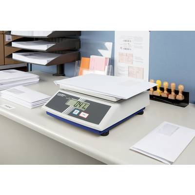 Scène de bureau avec une balance numérique pesant une lettre. Des casiers de documents et des tampons sont visibles en arrière-plan.