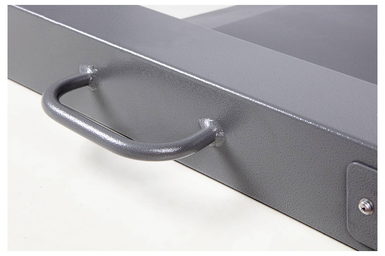 Poignée métallique sur un objet rectangulaire gris, probablement une boîte à outils ou un tiroir. La surface est légèrement texturée.