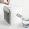 Un petit refroidisseur d'air à côté d'un verre d'eau. Une main effleure doucement le dessus du refroidisseur pour le faire fonctionner.
