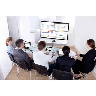 Un groupe de cinq personnes est assis autour d'une table dans une salle de conférence et regarde une grande présentation sur écran mural avec des diagrammes et des graphiques.