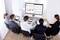 Un groupe de cinq personnes est assis autour d'une table dans une salle de conférence et regarde une grande présentation sur écran mural avec des diagrammes et des graphiques.