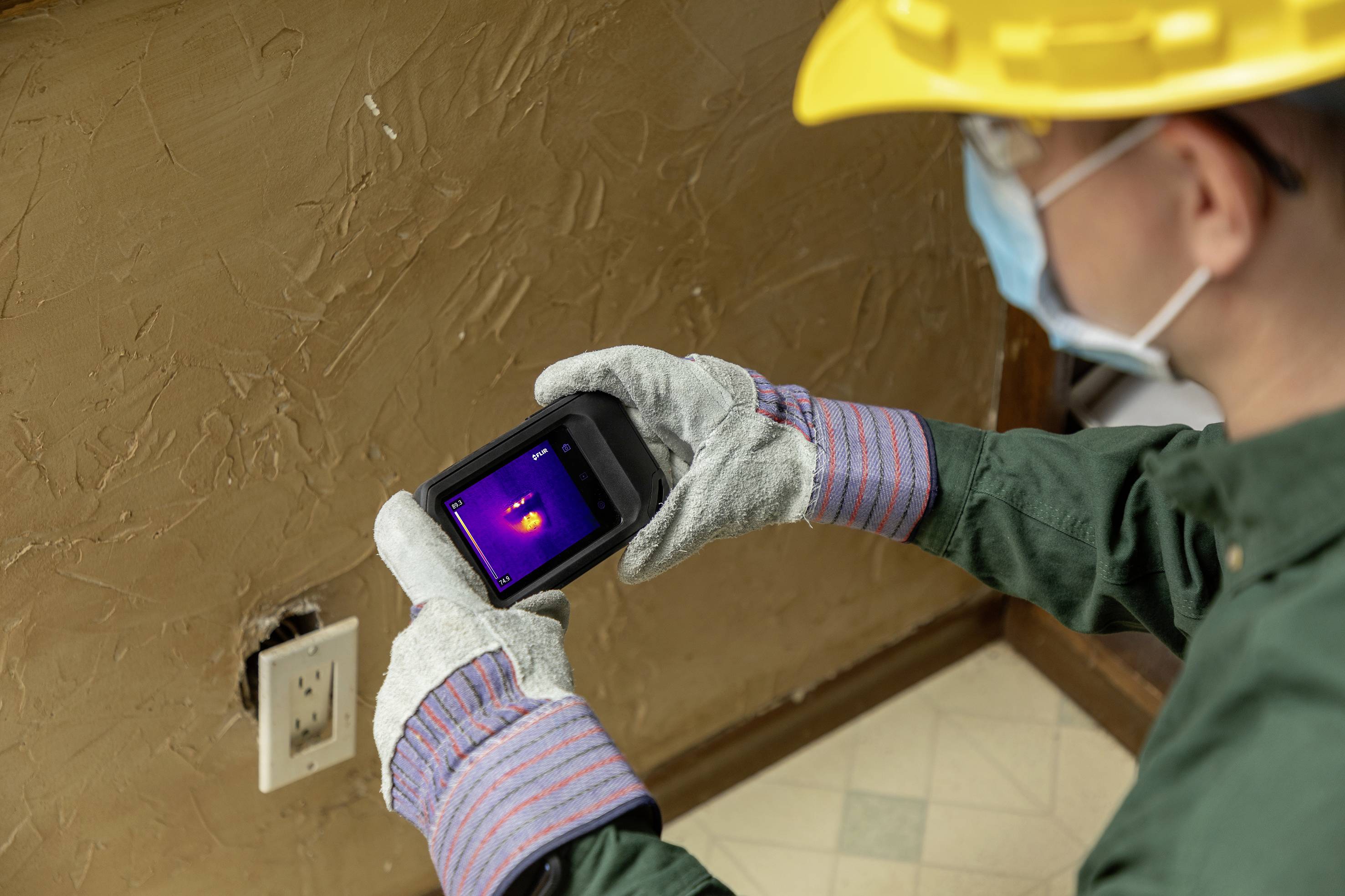Un technicien inspecte un mur à l'aide d'un thermomètre infrarouge, probablement à la recherche de pertes de chaleur ou d'humidité.
