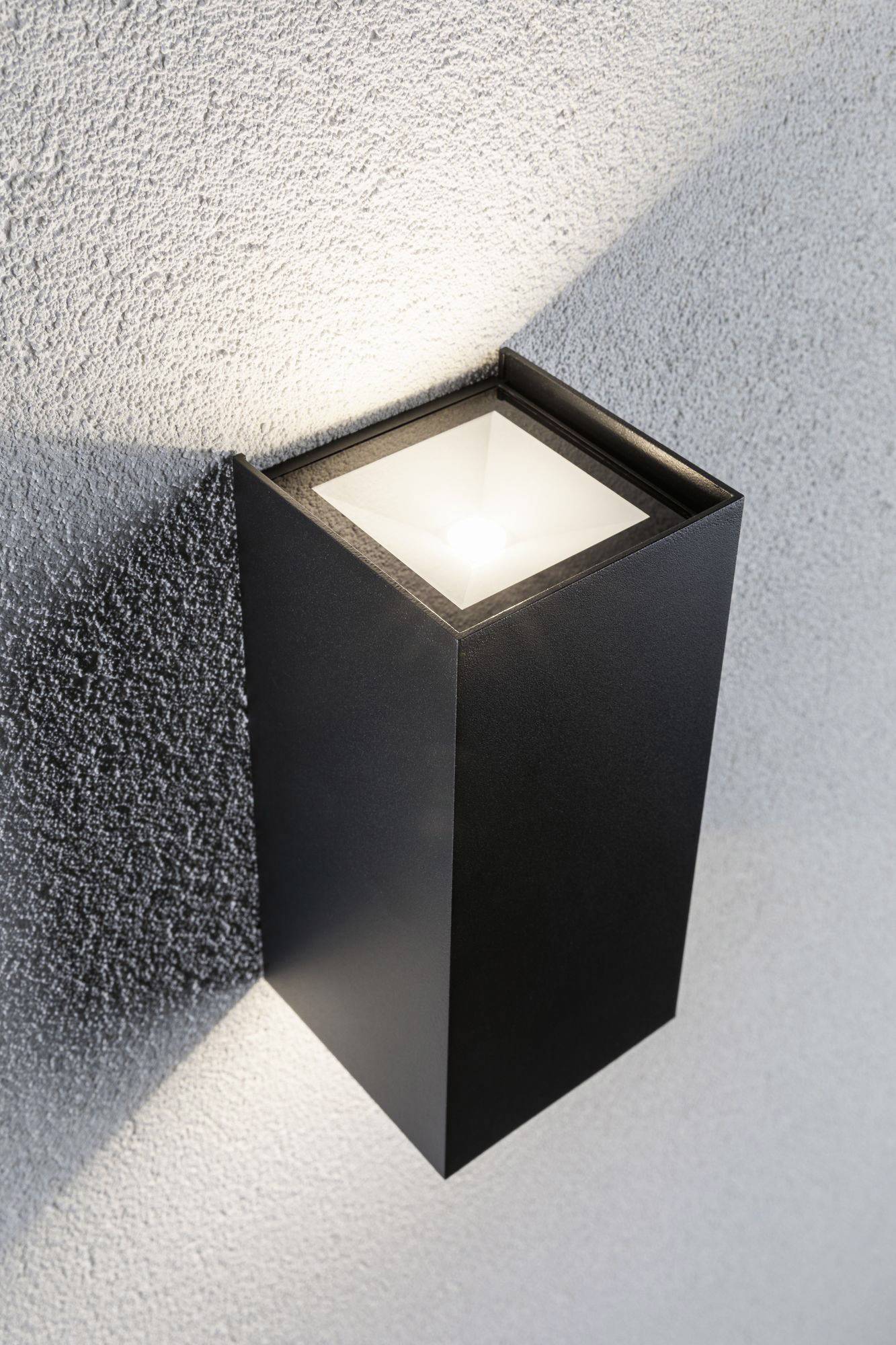 Luminaire extérieur moderne en forme de cube, monté sur un mur gris texturé. La lumière rayonne vers le haut et vers le bas.