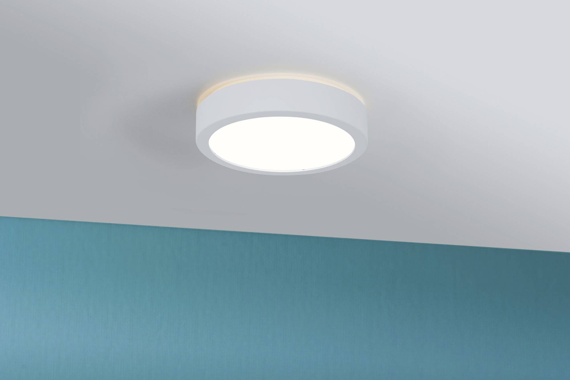 Une applique ronde blanche diffuse une lumière vive sur un mur peint en bleu.