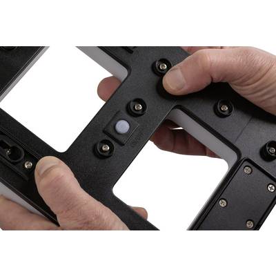 Deux mains tiennent un cadre rectangulaire noir avec plusieurs vis visibles.