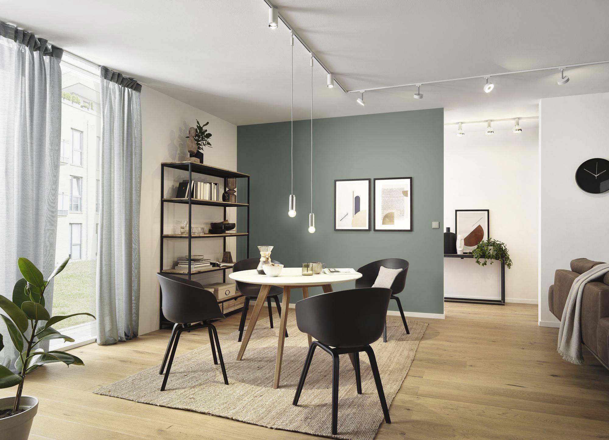 Salle à manger avec une table ronde, quatre chaises noires et une étagère. Mur d'accent vert avec deux tableaux. Design moderne et naturel.