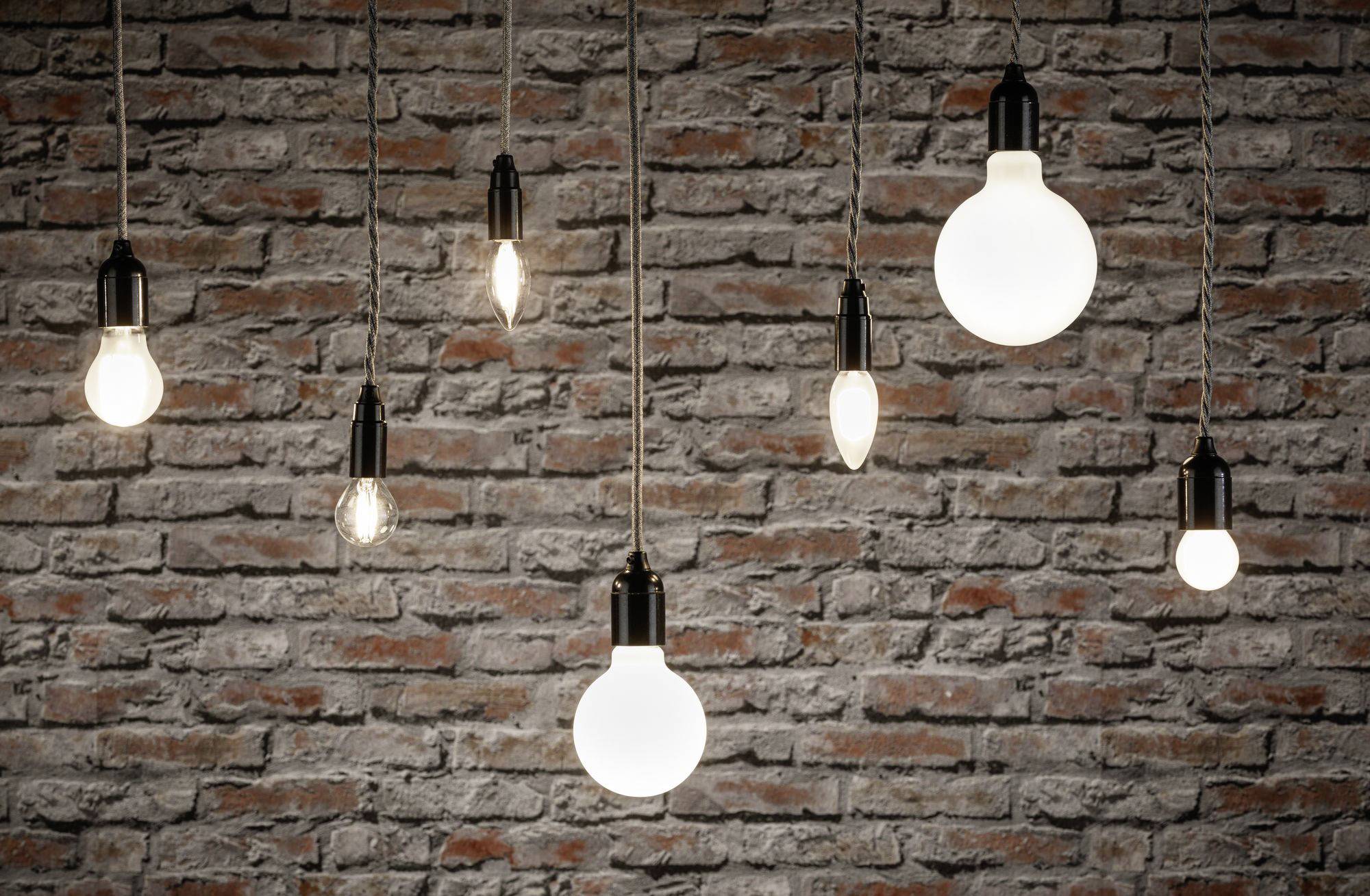 Différentes ampoules sont suspendues devant un mur de briques et brillent avec des intensités différentes. Elles créent une ambiance chaleureuse et atmosphérique.