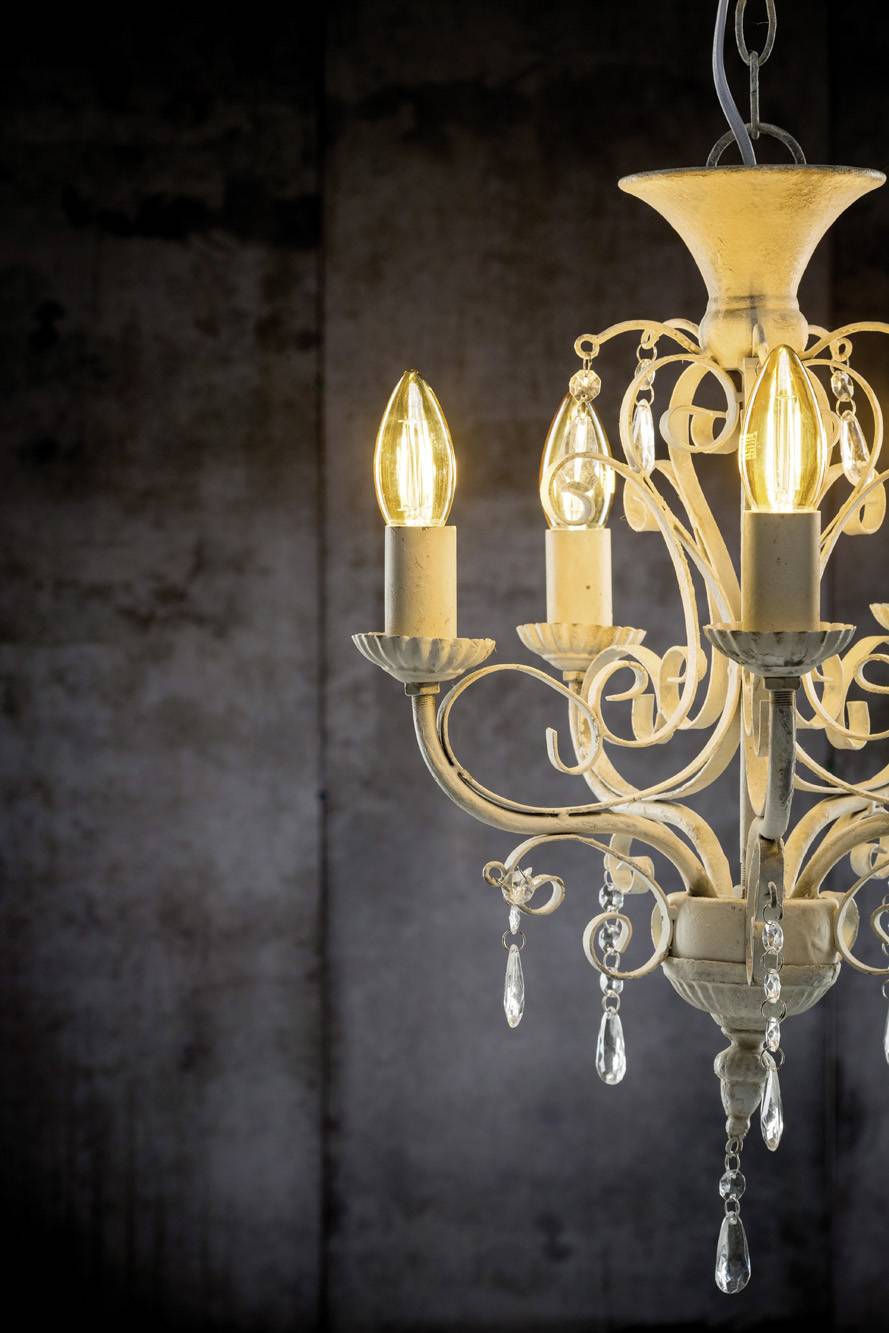 Un lustre élégant avec trois lampes à bougie allumées et des cristaux étincelants sur un fond sombre.