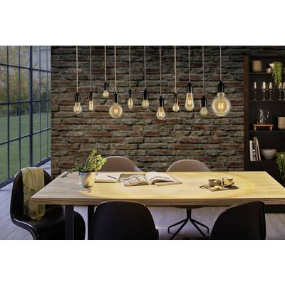 Un espace repas chaleureux avec une table en bois et des chaises noires, éclairé par plusieurs ampoules suspendues devant un mur de briques.
