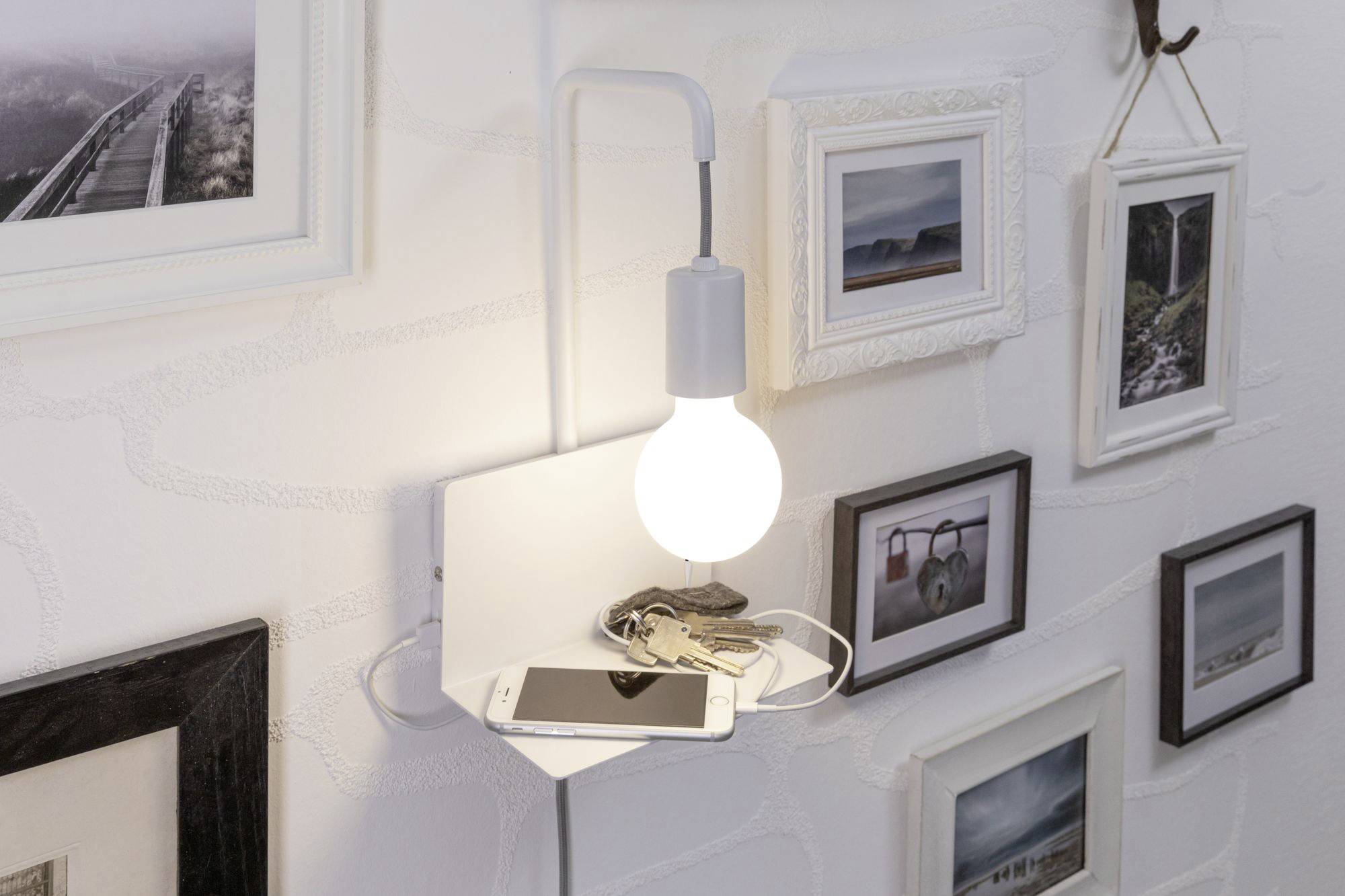 Une étagère avec une lampe, sur laquelle reposent un smartphone et des clés. Des cadres sont accrochés au mur.