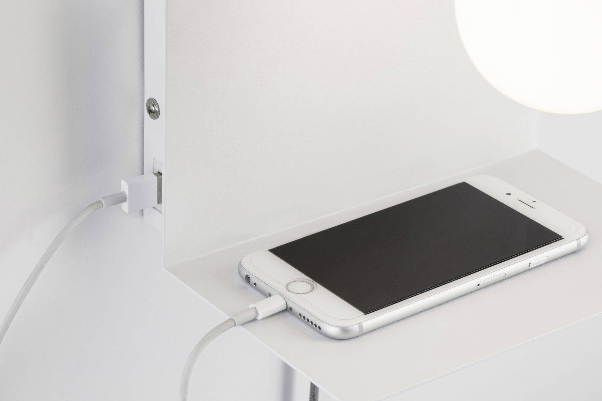 Un smartphone est posé sur une table et est en train de charger via un câble.