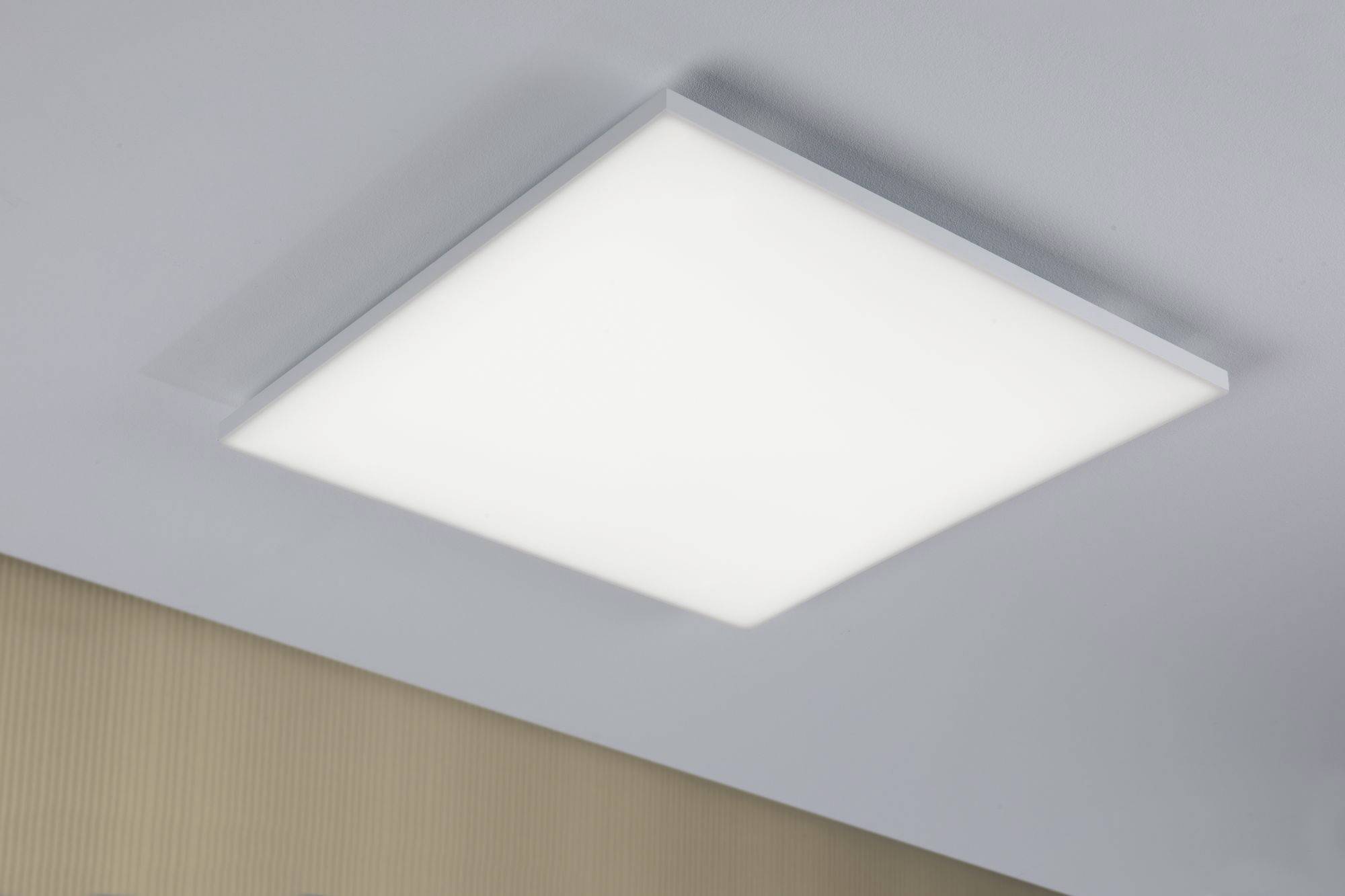Plafonnier LED carré, éclairage uniforme, installé sur un plafond blanc au-dessus d'un fond beige texturé.