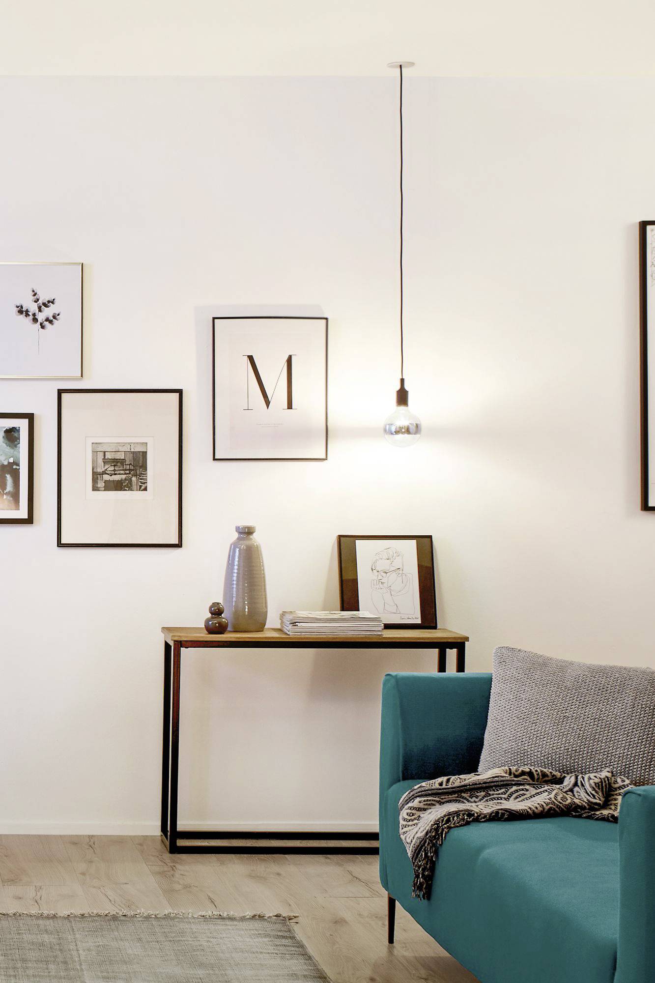 Un salon avec un canapé turquoise, surplombé par une lampe. Des cadres de différentes tailles sont accrochés au mur.