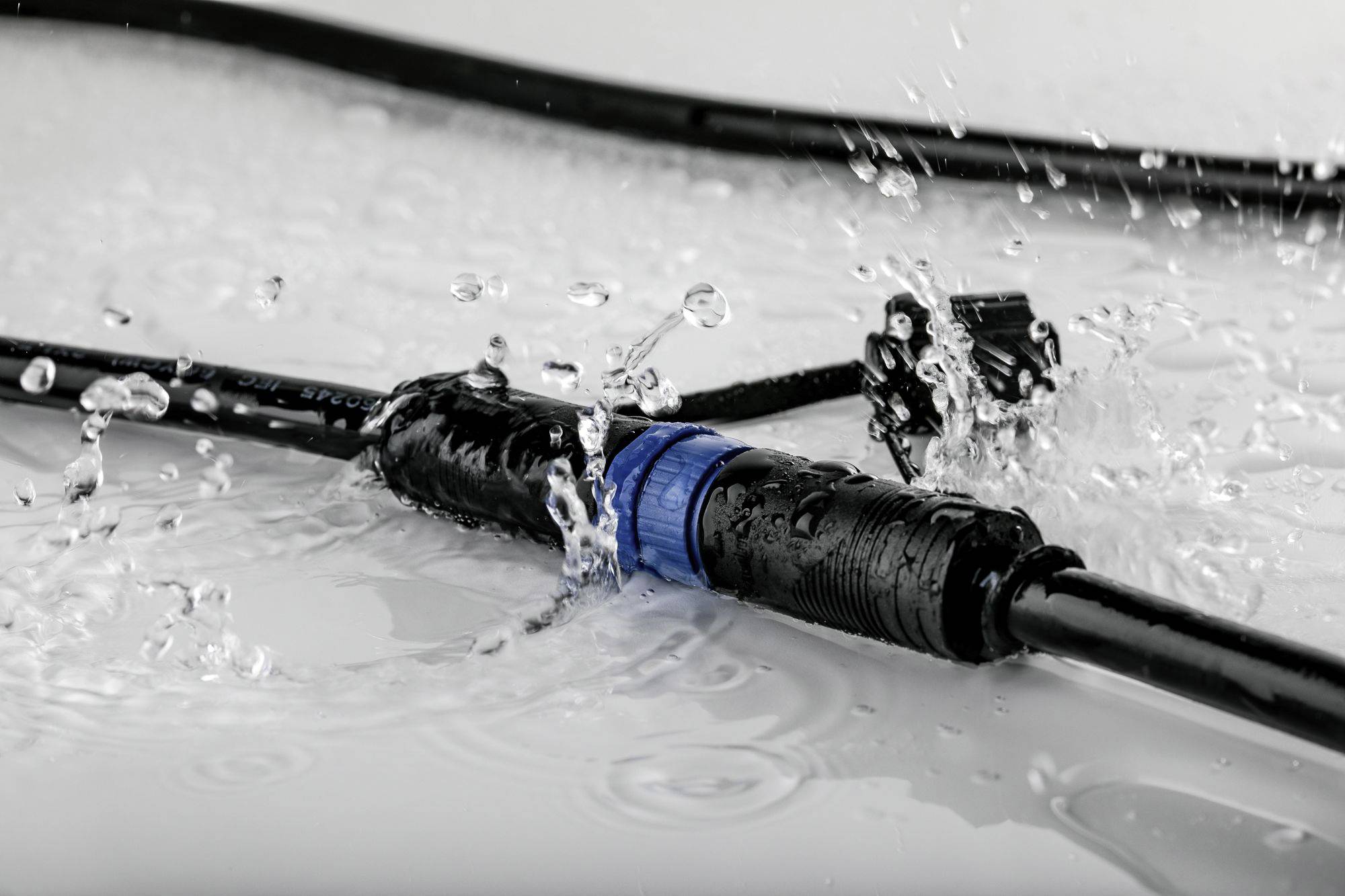 Un tuyau d'eau avec des raccords bleus et noirs est visible sur une surface humide. De l'eau jaillit autour de lui.