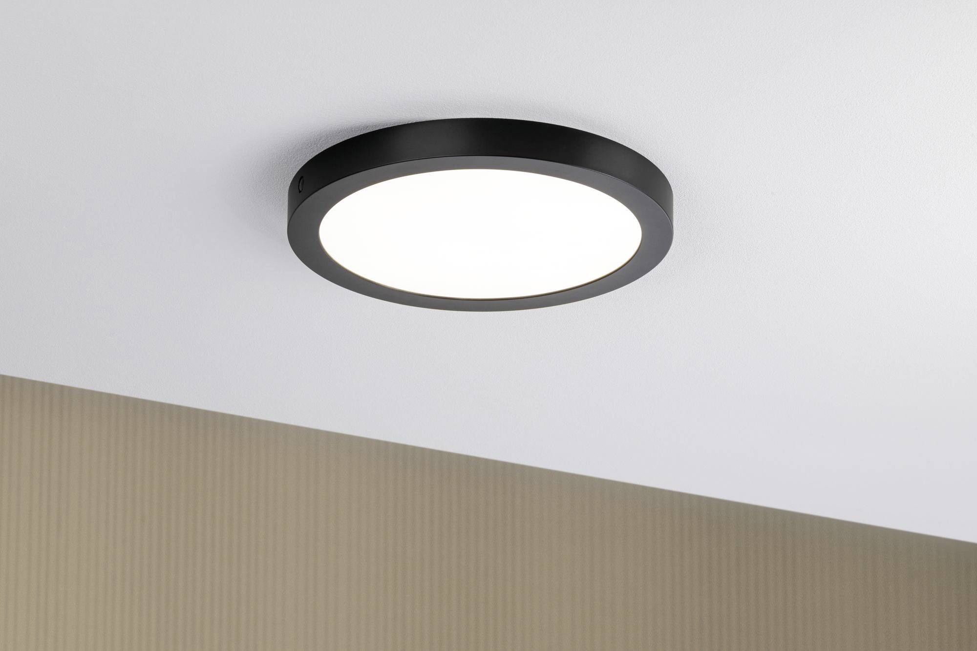 Un luminaire rond noir fixé au plafond blanc d'une pièce et qui éclaire.
