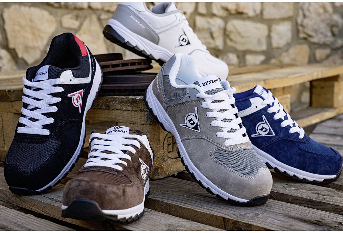 Cinq paires de chaussures de sport décontractées de différentes couleurs (noir, marron, gris, bleu, blanc) sont posées sur une palette en bois.