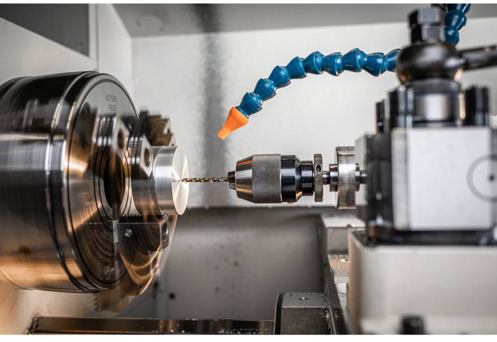 Un tour mécanique fore avec précision une pièce métallique. Un tube de liquide de refroidissement orange maintient le processus de forage au frais.