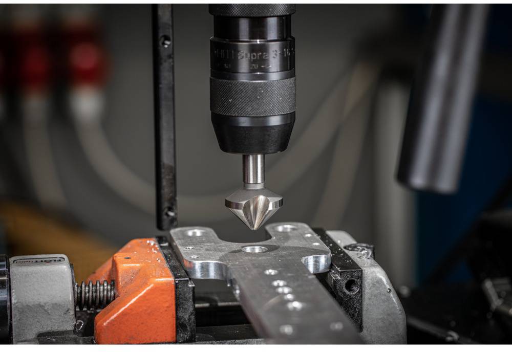 Gros plan d'une machine CNC usinant du métal ; un foret s'abaisse précisément dans une pièce. Environnement industriel en arrière-plan.