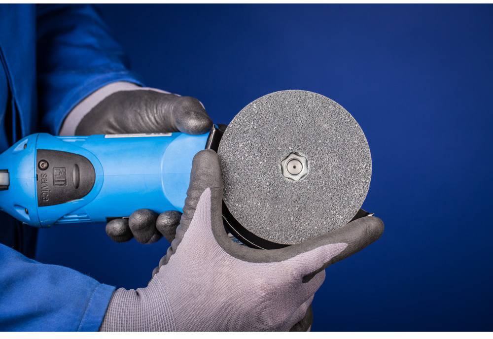 Une personne portant des gants de protection tient une meuleuse d'angle avec un disque de meulage dans un environnement bleu.