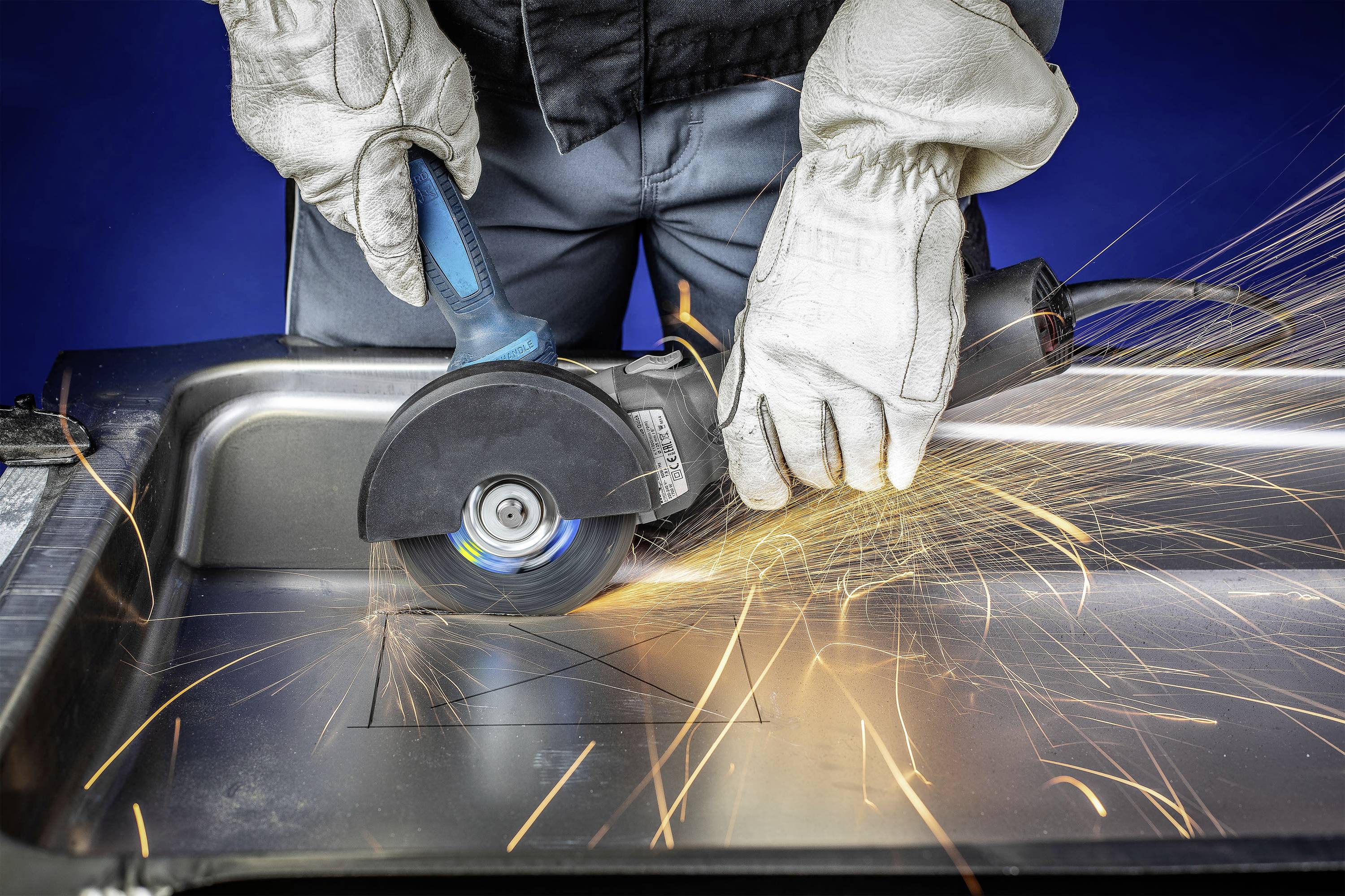 Une personne coupe du métal avec un meuleuse d'angle. Des étincelles volent sur une surface en acier inoxydable. Des gants de protection sont portés.
