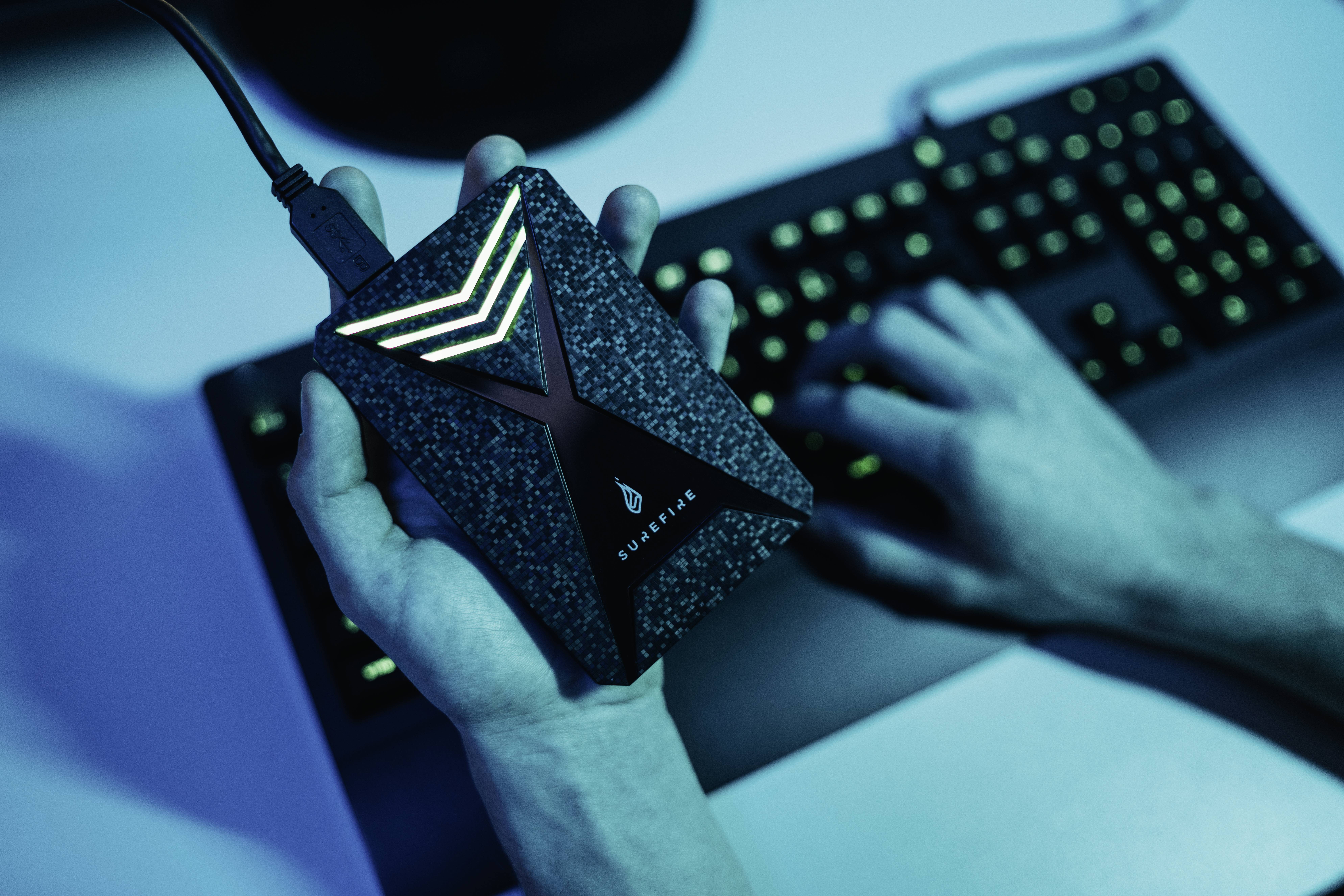 Une personne tient un disque dur externe devant un clavier rétroéclairé. La scène est baignée de lumière bleue.