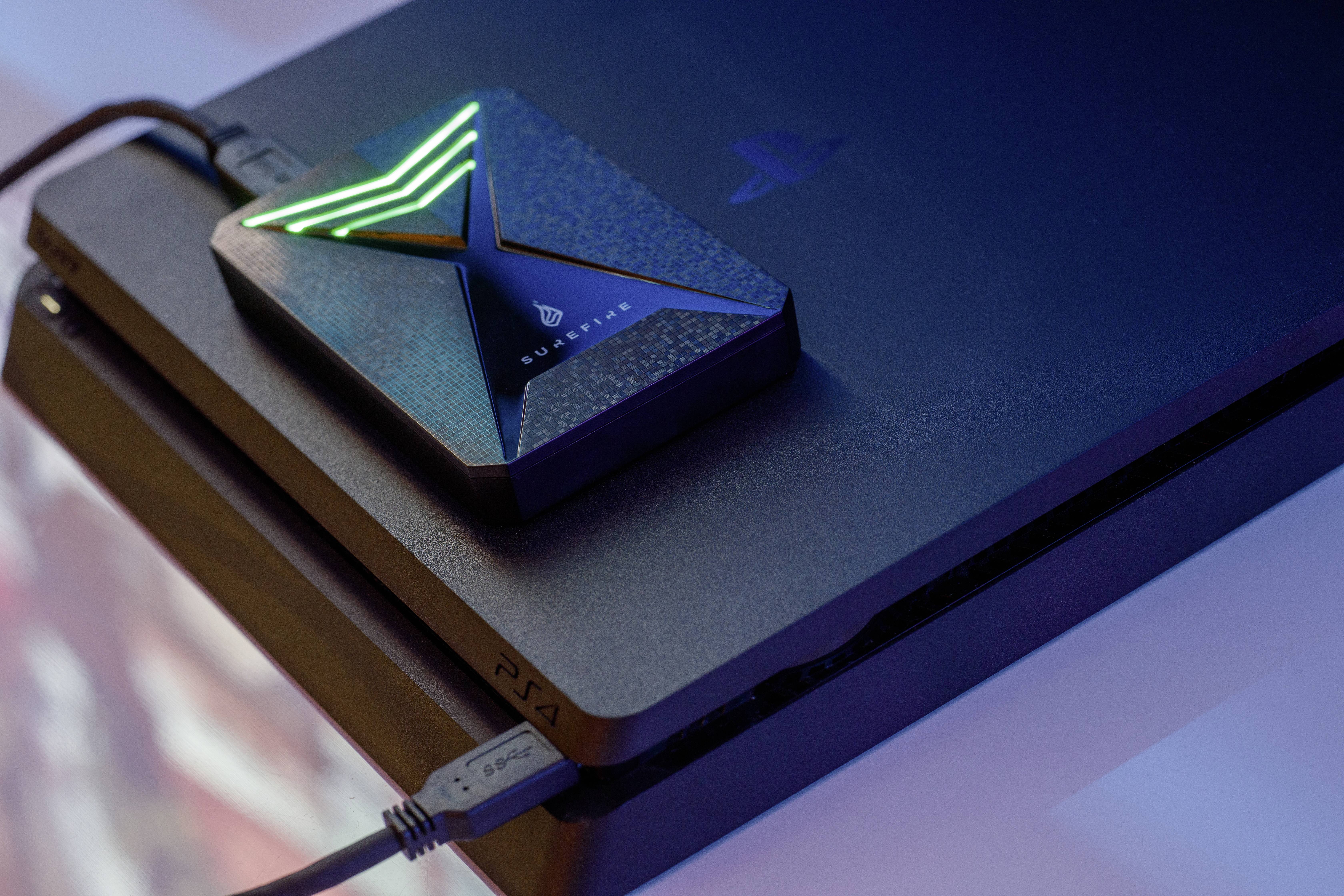 Disque dur externe avec un motif X lumineux posé sur une console de jeux, connecté via un câble USB.