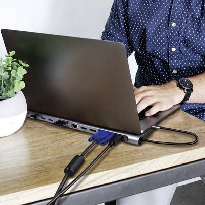 Une personne travaille sur un ordinateur portable à une table, regardant l'écran. Une petite plante est posée à côté.