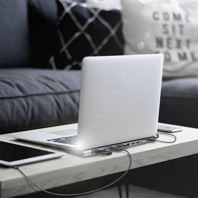 Un ordinateur portable est posé sur une table, avec un hub USB connecté. Un canapé avec un coussin est visible en arrière-plan.