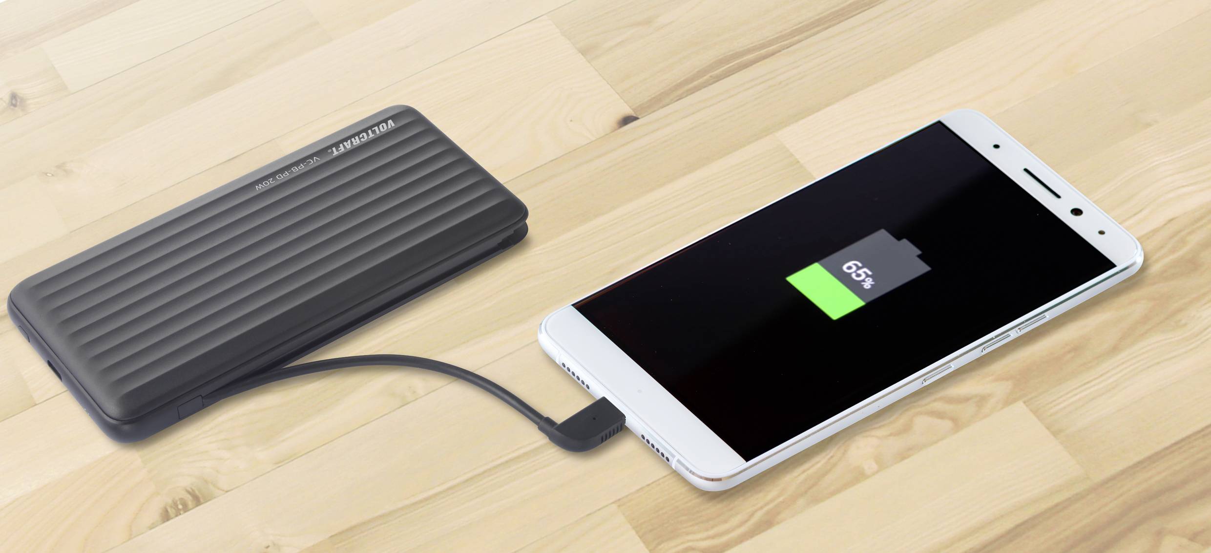 Un smartphone est en train d'être chargé par une batterie externe noire reliée par un câble. L'écran affiche un niveau de batterie de 65 %.