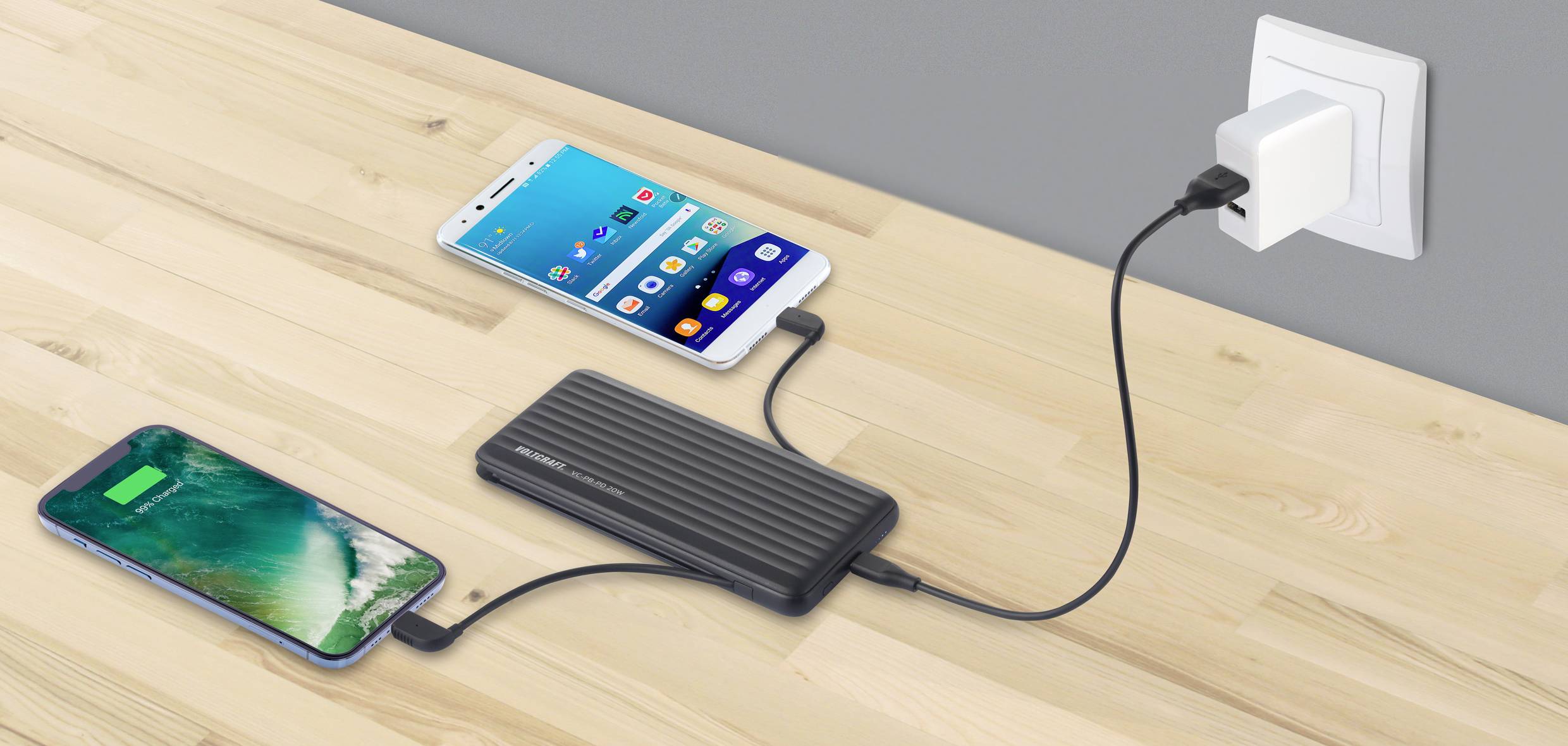 Deux smartphones sont en train de charger sur un chargeur branché dans une prise électrique sur une table en bois.