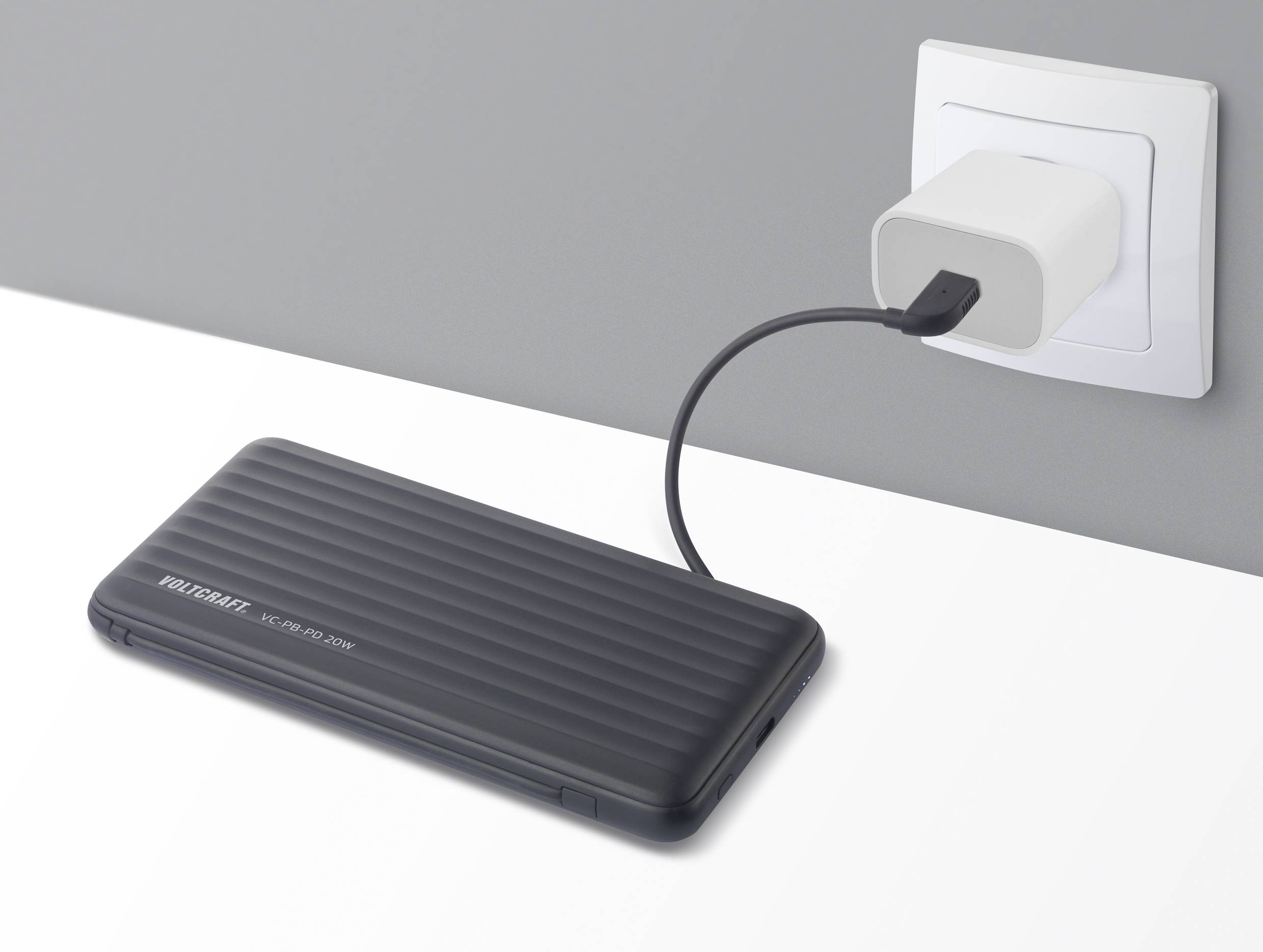 Un câble de charge mobile relie un disque dur externe noir à une prise électrique blanche sur le mur.
