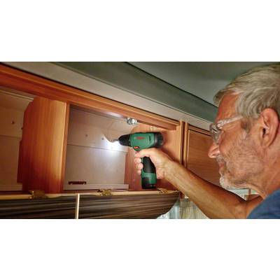 Un homme utilise une visseuse sans fil verte pour installer une étagère dans un camping-car. L'accent est mis sur l'activité artisanale.